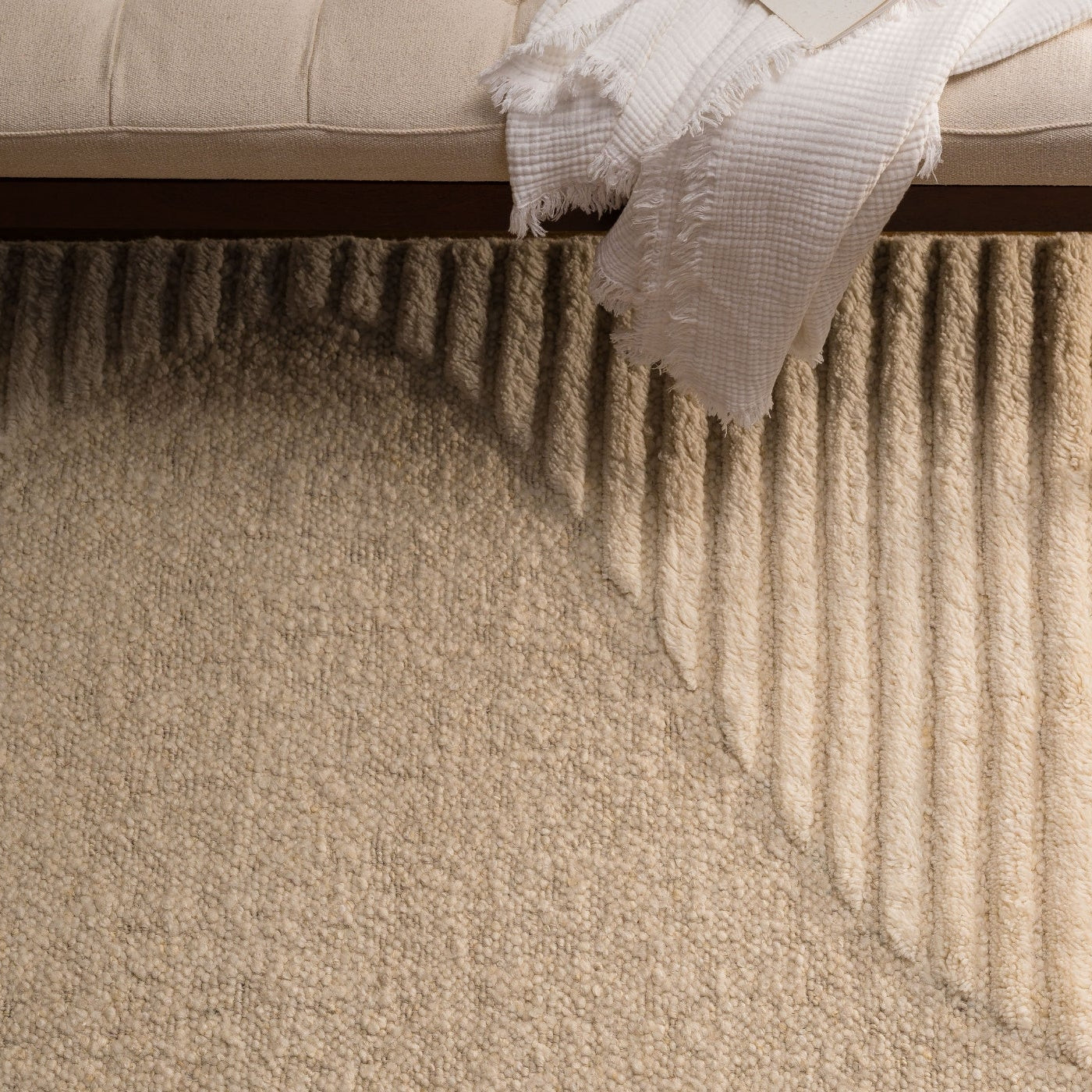 Close-up of a textured beige carpet with a bench and white fabric in the background.